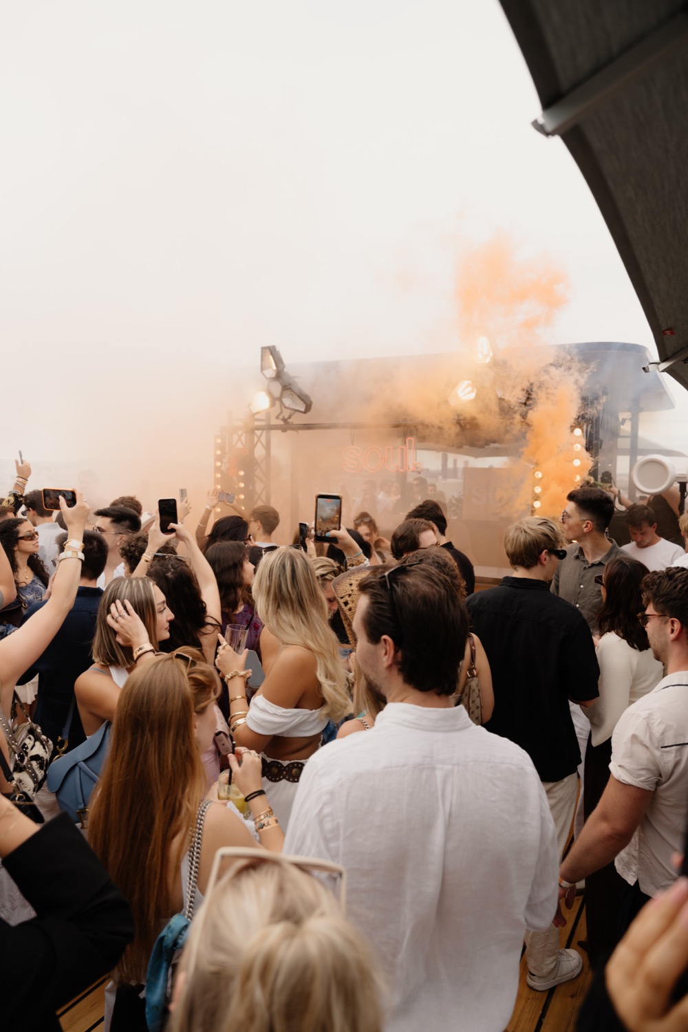 Crowd at a rooftop event with smoke and lights